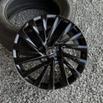 Black multi-spoke car wheel with Toyota center cap on gravel driveway
