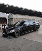Black BMW sedan with sporty wheels parked at an industrial train yard under a covered platform