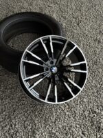 BMW alloy wheel with a black and silver split-spoke design resting next to a tire on gravel surface.