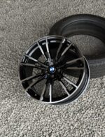 Black BMW alloy wheel with many spokes lying on a gravel surface beside a tire.