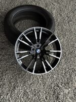 BMW alloy wheel with black and silver spokes placed on a gravel surface, tire in the background.