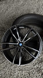 Black BMW alloy wheel with silver accents lying on a gravel surface beside a tire