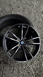 BMW alloy wheel with black and silver spokes resting on gravel beside a tire