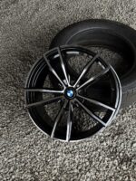 BMW alloy wheel with black and silver spokes resting on a tire on a gravel surface, center BMW logo visible