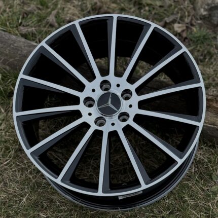 Round multi-spoke Mercedes alloy wheel with a silver rim on grass, center cap shows the Mercedes logo.
