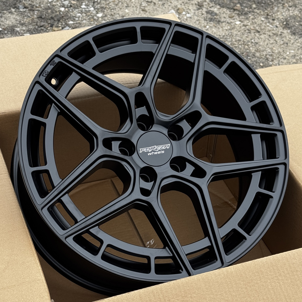 DSK-R19-5x112-439a94_0-2 Black matte finish alloy wheel with a multi-spoke design, centered in a cardboard box; center cap reads 'Forza Wheels'.