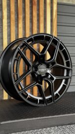 Black, high-gloss aftermarket alloy wheel with a geometric, multi-spoke design resting against wooden slats