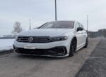 White Volkswagen sedan with black rims parked on a snowy roadside, facing left.
