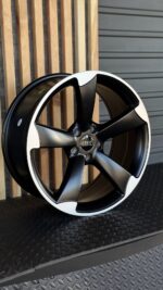 Close-up of a two-tone Audi alloy wheel with five black spokes and a white outer lip, center cap shows the Audi logo.