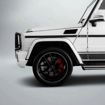 Front-left profile of a white Mercedes-Benz AMG G-Class, highlighting the wheel with black spokes and red brake calipers in a studio setting