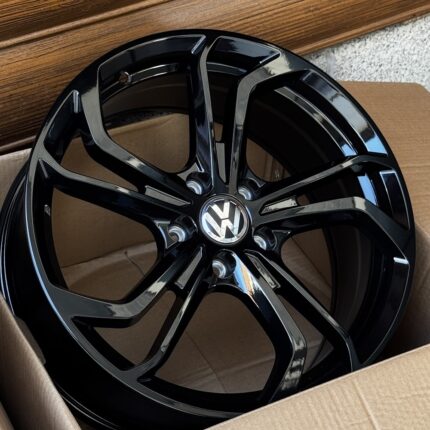 Black glossy Volkswagen alloy wheel with a five-spoke split design, in a cardboard box.