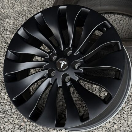 Black Tesla alloy wheel rim with a multi-spoke design on a gravel surface