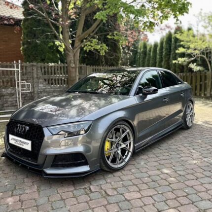 Gray Audi sedan parked on a stone driveway with aftermarket large alloy wheels and yellow brake calipers.