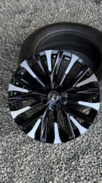 Black and silver multi-spoke Toyota alloy wheel with a mounted tire on a gravel surface