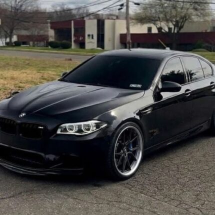 Black BMW sedan photographed from the front-left, parked on a street with tinted windows and aftermarket wheels.