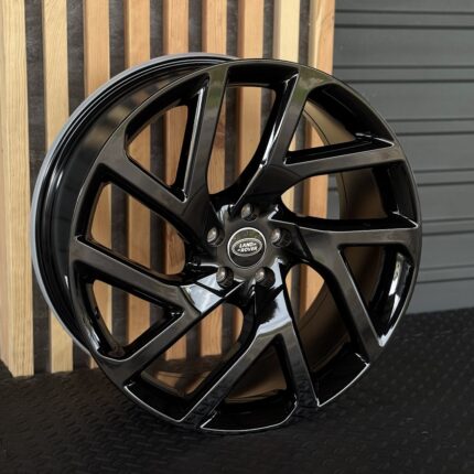 Glossy black alloy wheel with five split spokes and a Land Rover center cap on a dark floor.
