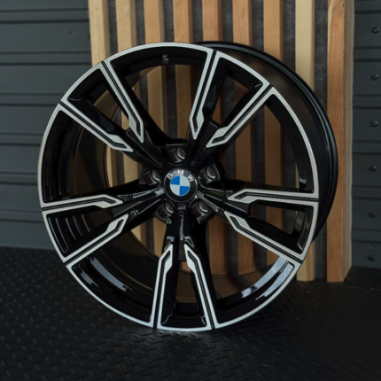 BMW alloy wheel with black finish and silver accents, displayed against a wooden slat backdrop.