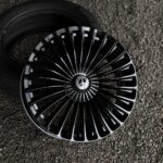 Black multi-spoke alloy wheel with a Mercedes-Benz center cap lying on gravel surface