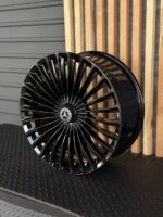 Glossy black multi-spoke Mercedes-Benz alloy wheel leaning against a wooden slat wall, center emblem visible.