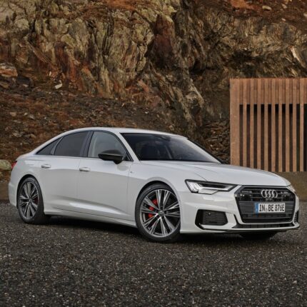 White Audi sedan parked on gravel with a rocky cliff behind it.