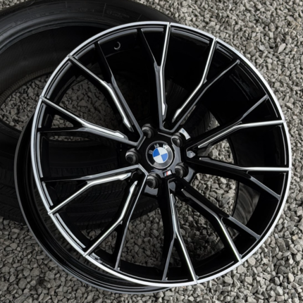 Close-up of a glossy black BMW alloy wheel with silver spokes on a gravel surface
