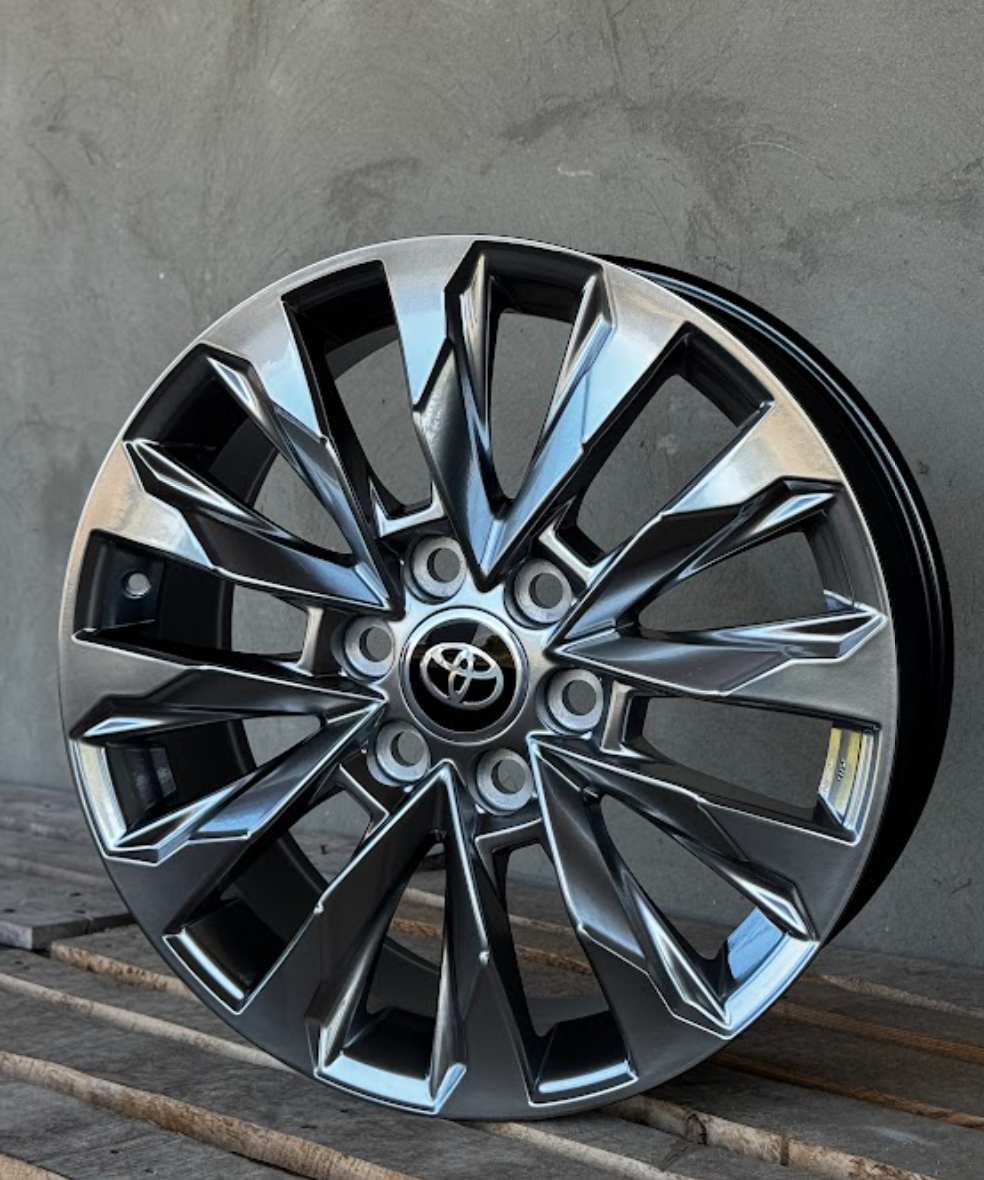 DSK-R20-6x139-7-b418c6_0-1 Chrome multi-spoke alloy car wheel with Toyota center cap leaning against a gray wall.