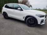 White BMW SUV with black alloy wheels parked on a paved surface, three-quarter front view.