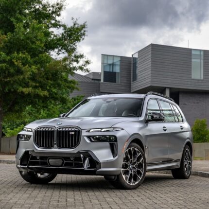 Silver BMW SUV parked on a brick driveway with a modern building and greenery in the background.