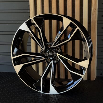 Audi alloy wheel with black and silver multi-spoke design, center cap featuring the Audi logo, resting against a wooden backdrop