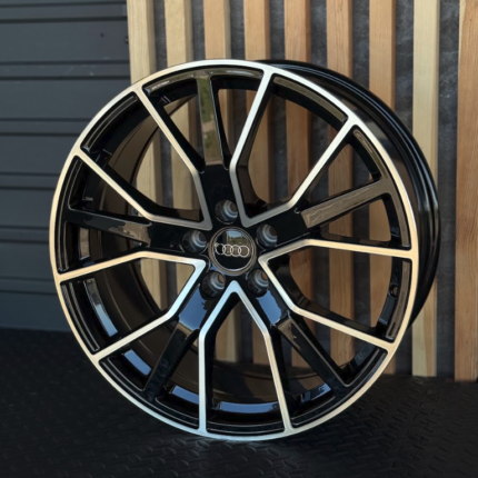 Black Audi alloy wheel with a multi-spoke design and silver accents, resting against wooden slats.