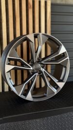 Audi alloy wheel with a bold, angular multi-spoke design and an Audi center cap against a wooden backdrop