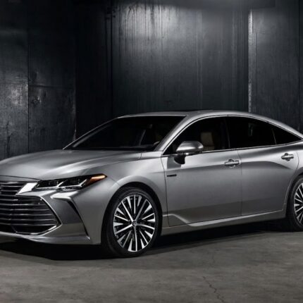 Silver Toyota sedan in a dark industrial garage, front-left three-quarter view.