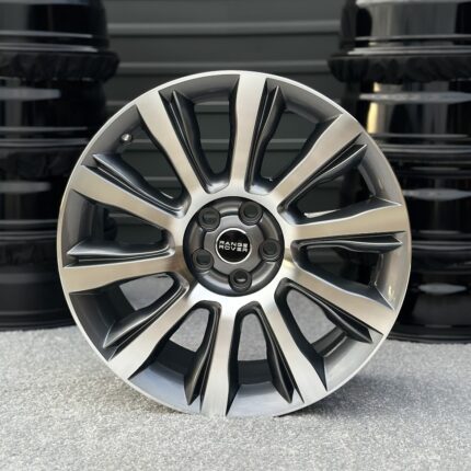 Close-up of a silver alloy wheel with a Range Rover center cap, with stacked tires in the background.