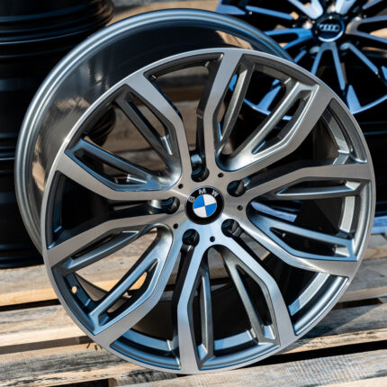 Close-up of a silver BMW alloy wheel with intricate spokes and the BMW emblem at the center, resting on a wooden pallet.