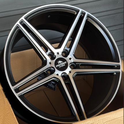 Black and silver five-spoke alloy car wheel in an open cardboard box, showing a machined finish and center cap.
