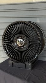 Black multi-spoke alloy wheel with chrome center cap reading Range Rover on a display stand against a gray wall.